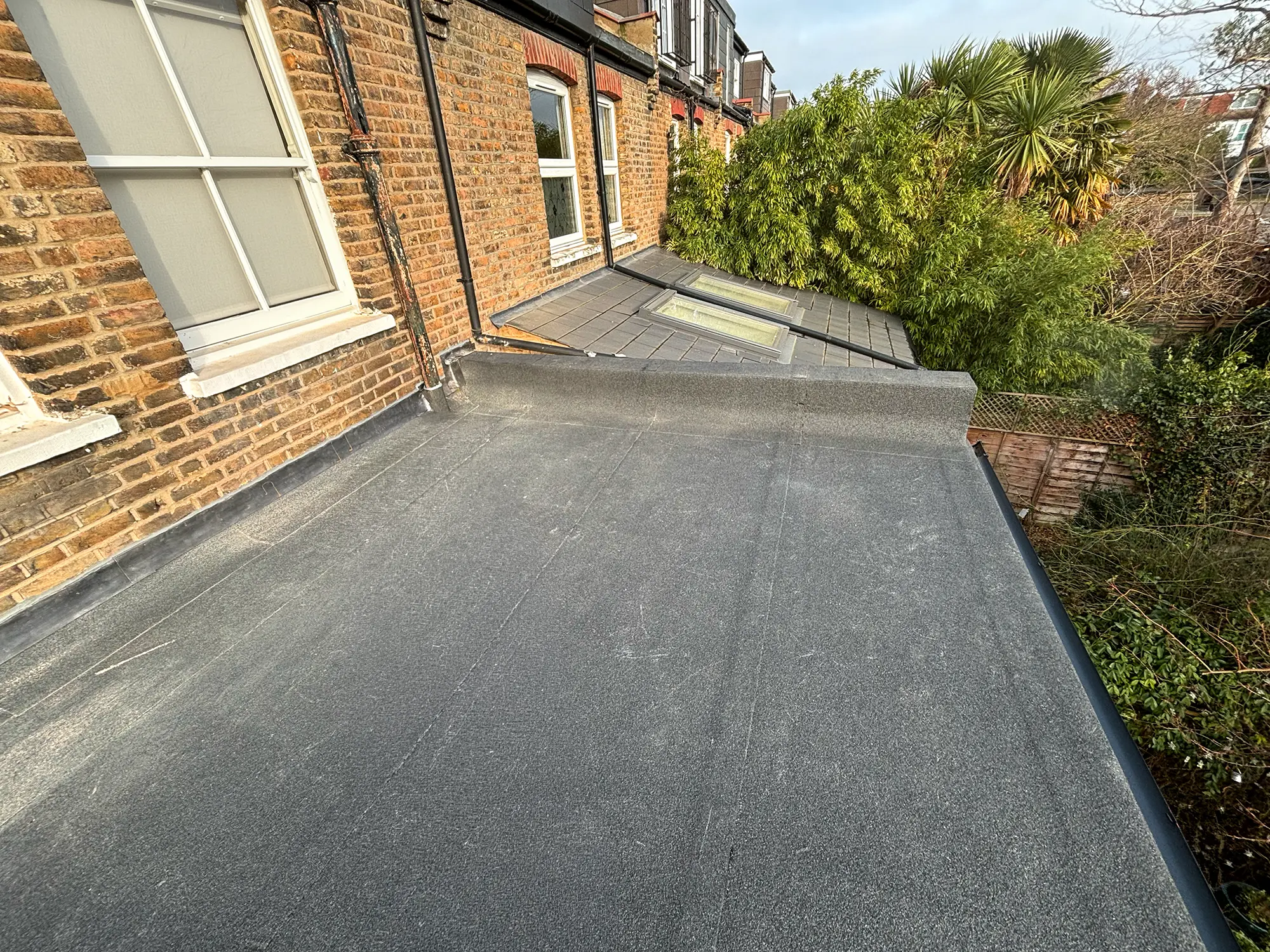 Flat roof with dark mineral felt on a brick extension, pitched roof and skylights beyond